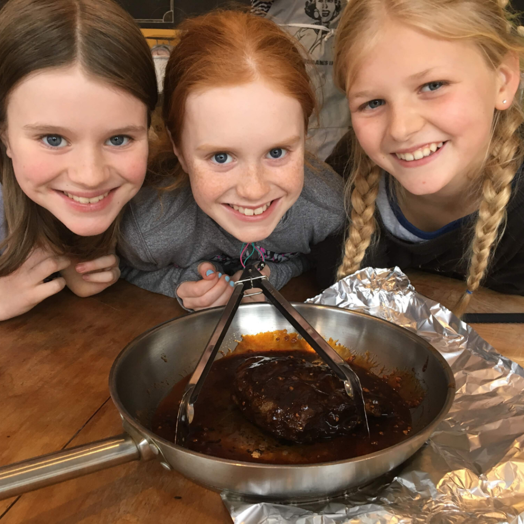 three tween girls smiling over a cooked steak