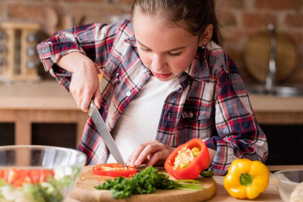 Young girl with plaid shirt cutting vegetables